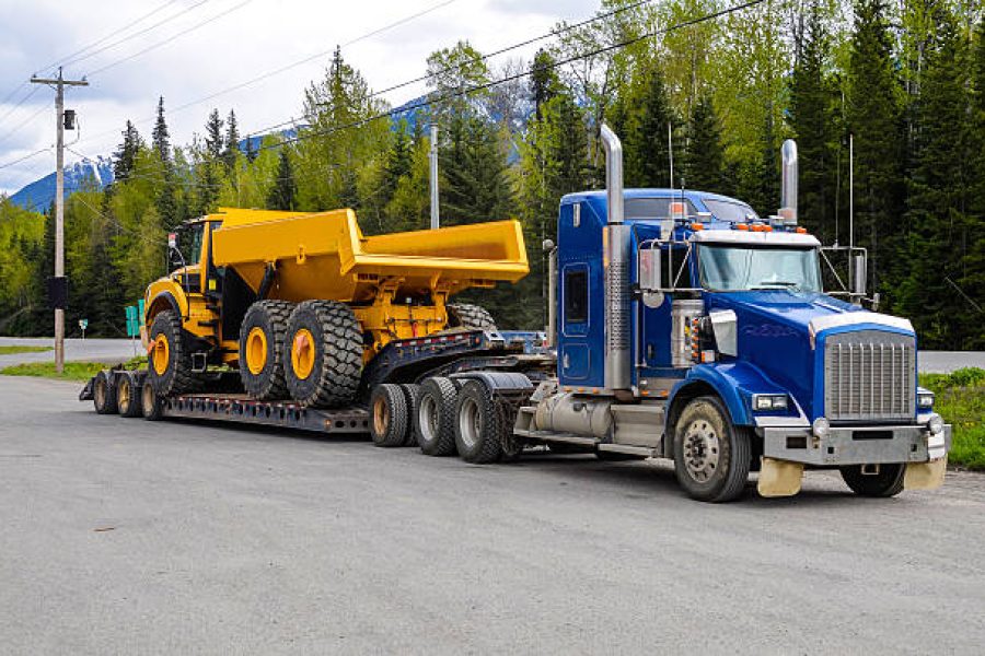 Big truck with a low platform trailer carrying a tipper truck on a public parking area of a truck stop